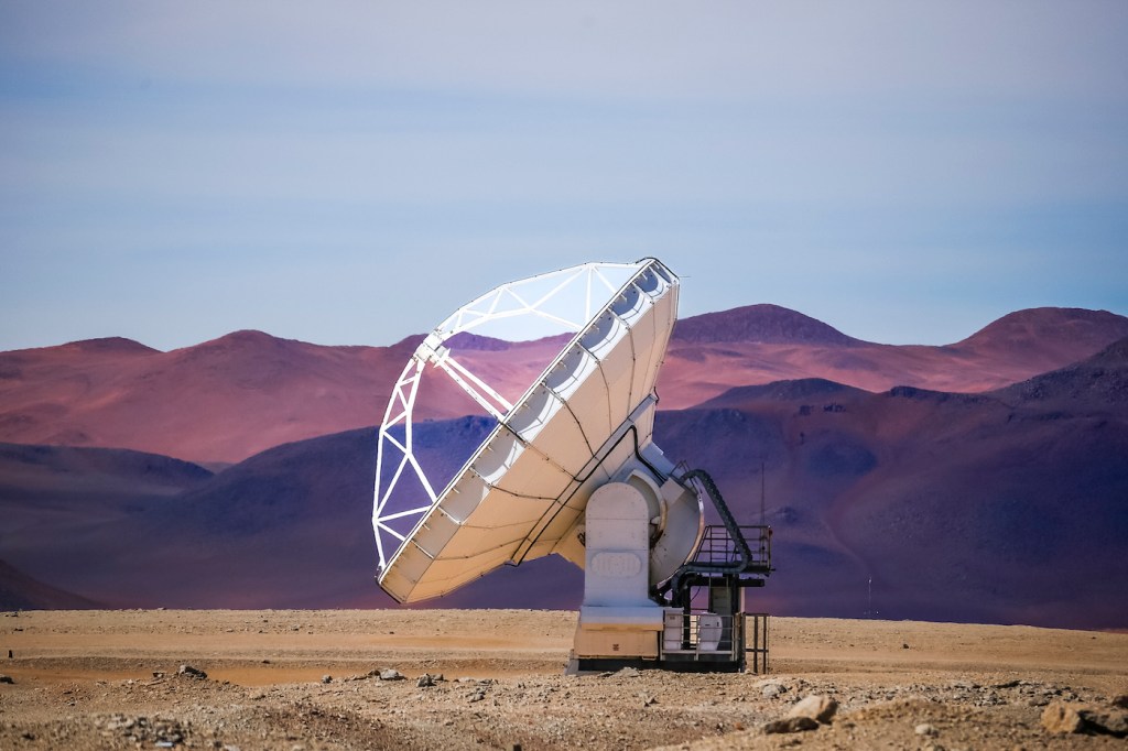 A satellite pointed up at the sky, with purple mountains in the background.